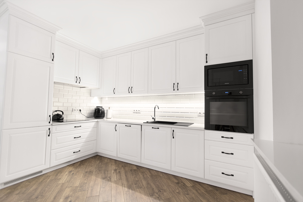 funkcjonalna biała kuchnia na wymiar z zabudową do sufitu i drewnianą podłogą – zdjęcie wnętrza dla producenta mebli kuchennych