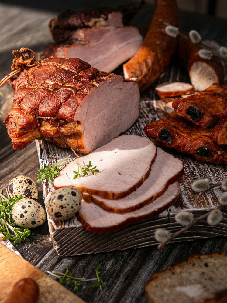 Szynka wielkanocna w plastrach z baziami – stylizowane zdjęcie jedzenia na desce.